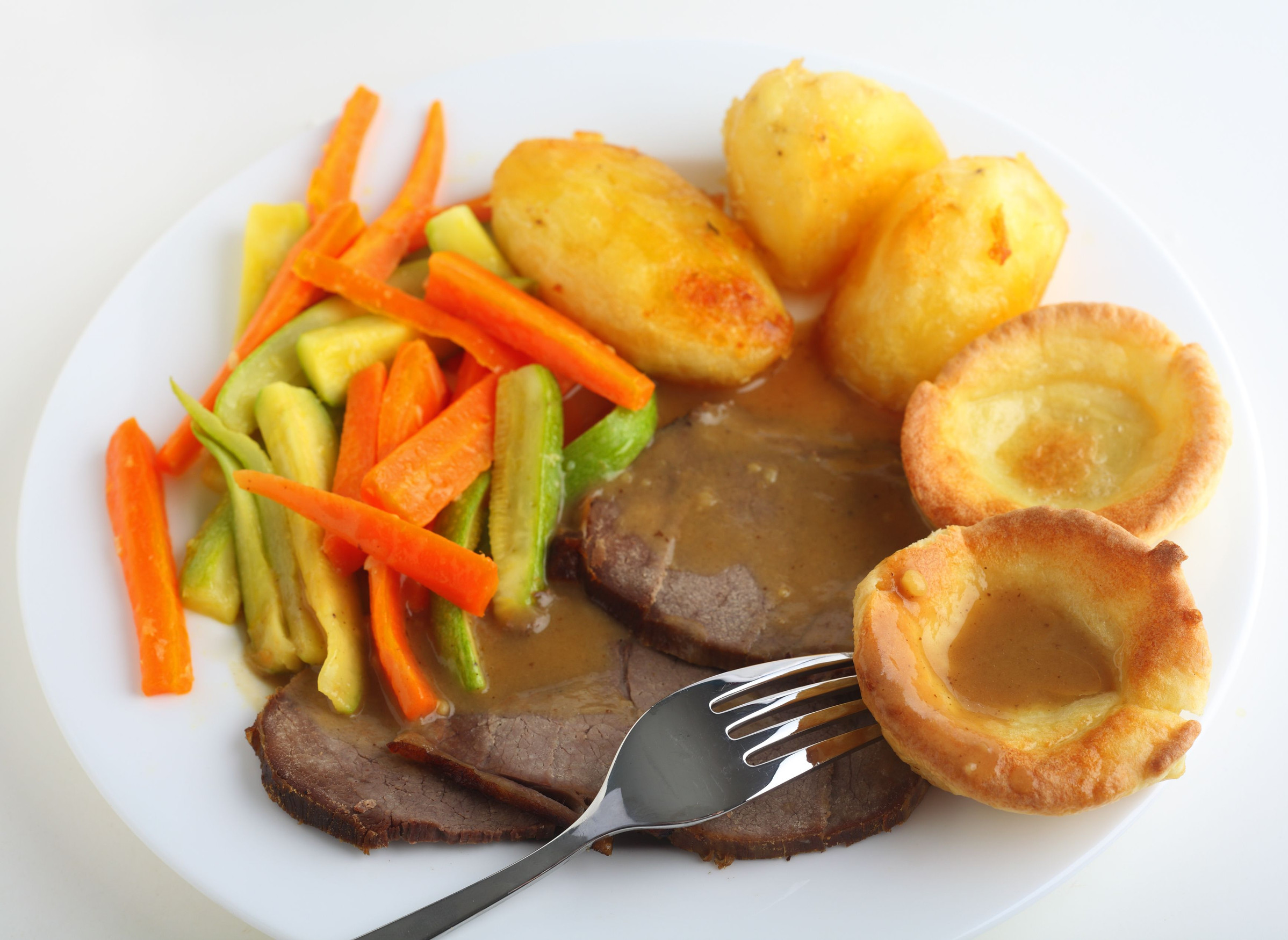 A plate of food with roast beef, vegetables, and Yorkshire pudding