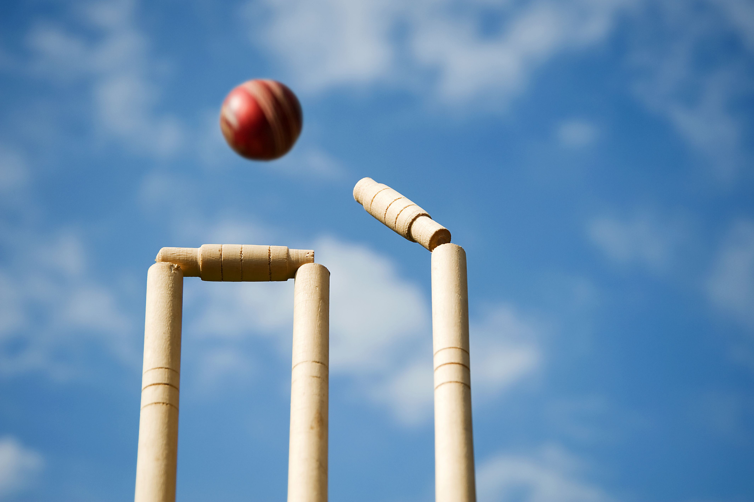 Cricketball trifft Stümpfe und löst sich vor blauem Himmel