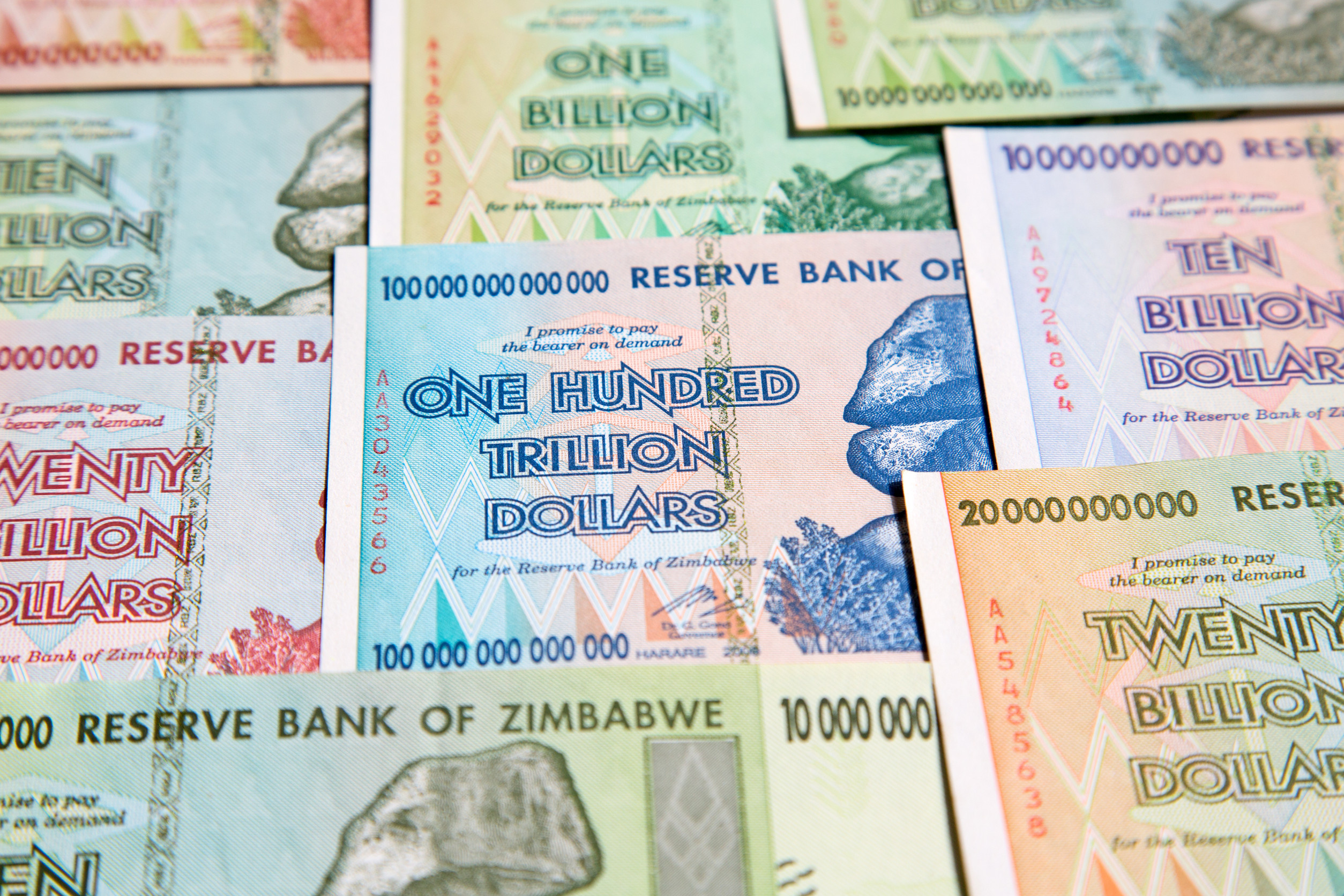 A close-up photo of a pile of colorful Zimbabwean banknotes, with denominations ranging from one billion to one hundred trillion dollars