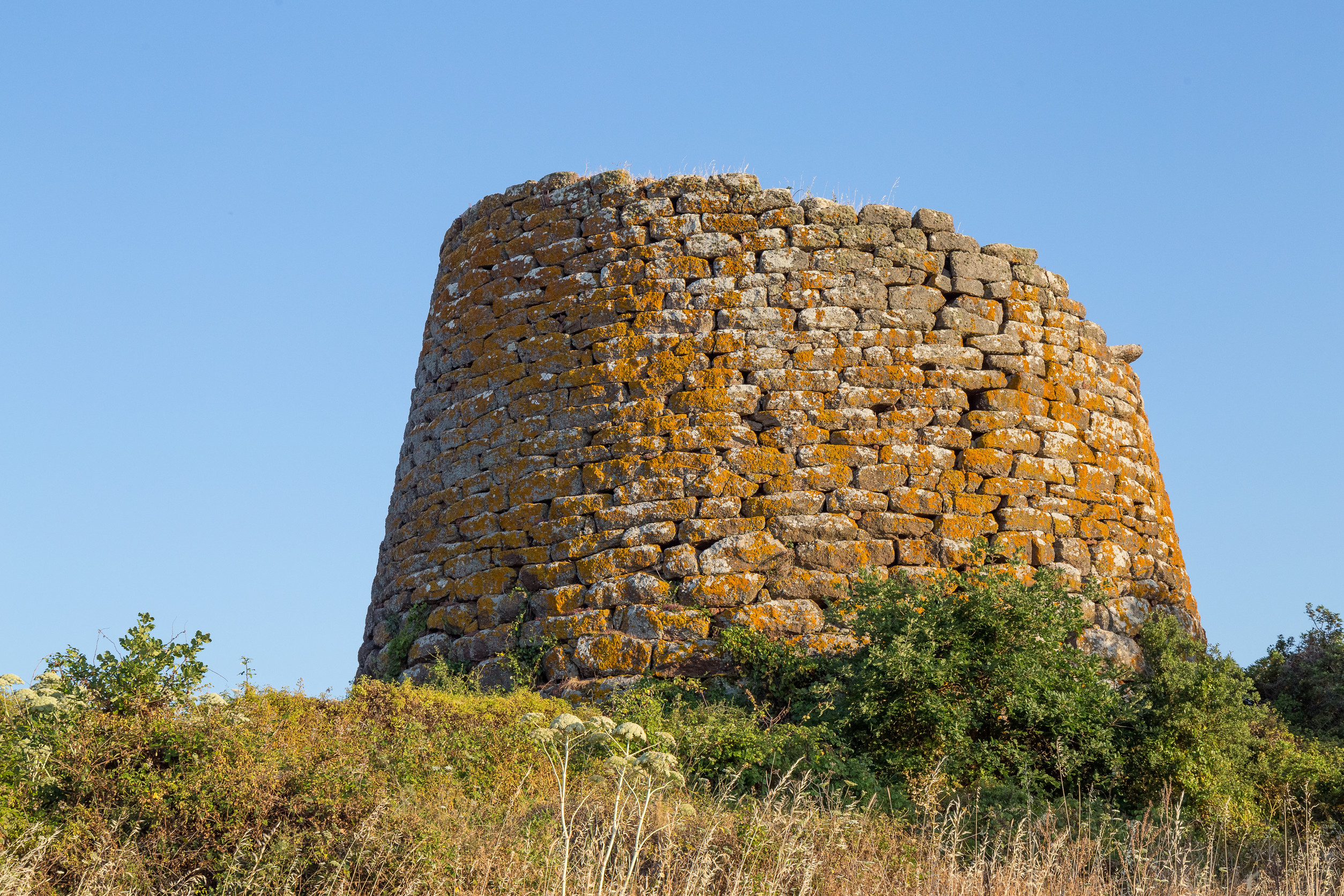 Ancient stone tower with orange lichen against clear blue sky