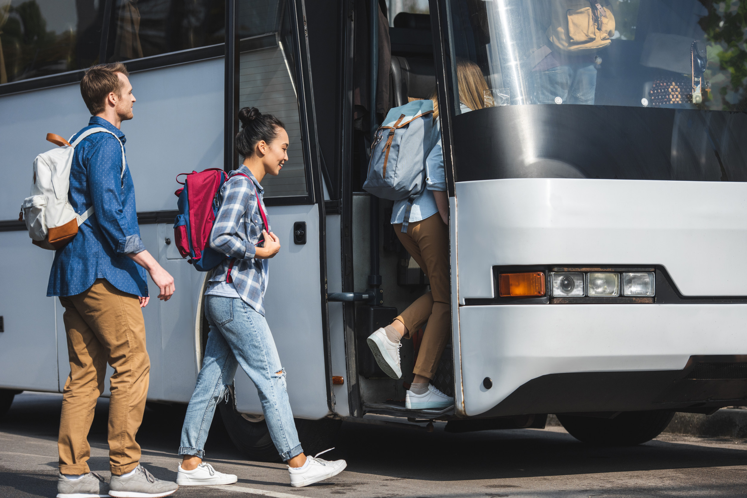 Young travelers with backpacks boarding a white tour bus