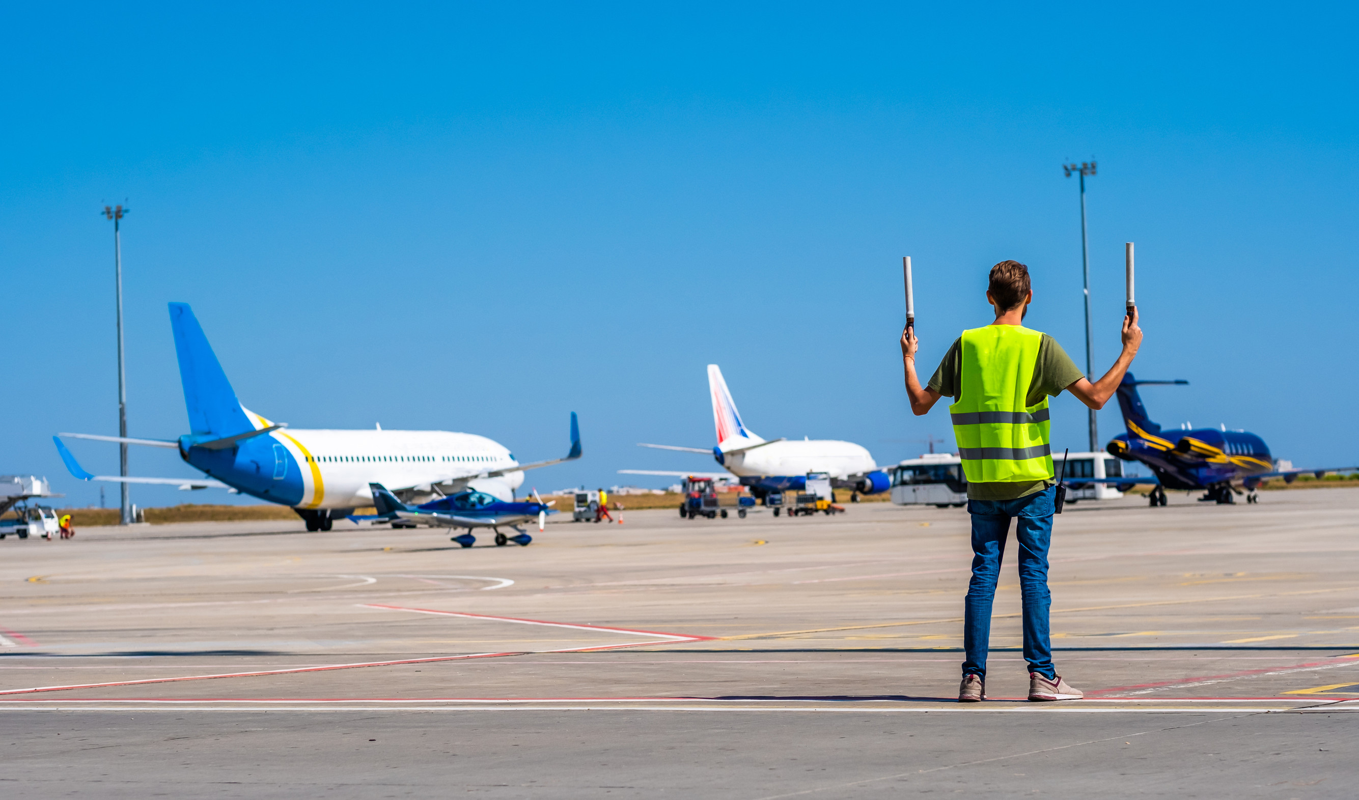 Airport ground crew guiding airplanes with signal wands on tarmac