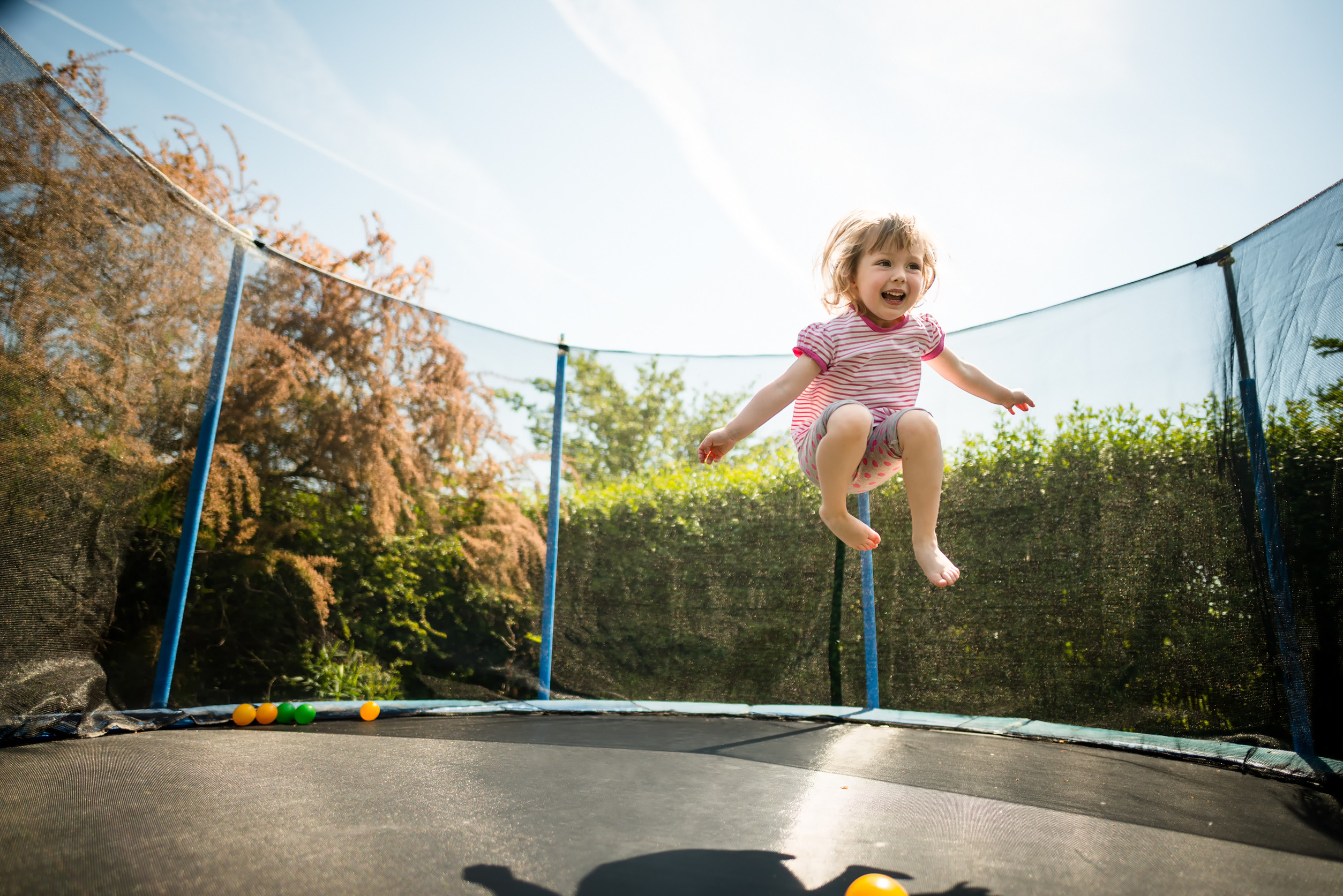 Glückliches junges Mädchen springt auf einem Trampolin in einem sonnigen Hinterhof