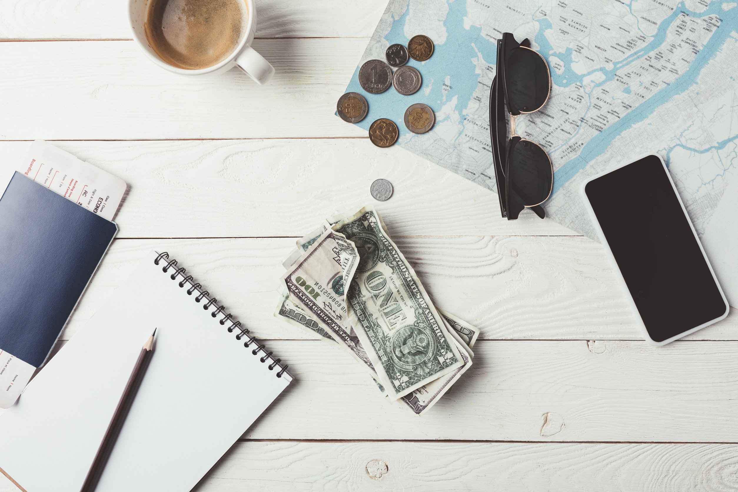 Argent, tasse à café, crayon, carte, passeport et téléphone sur une surface blanche