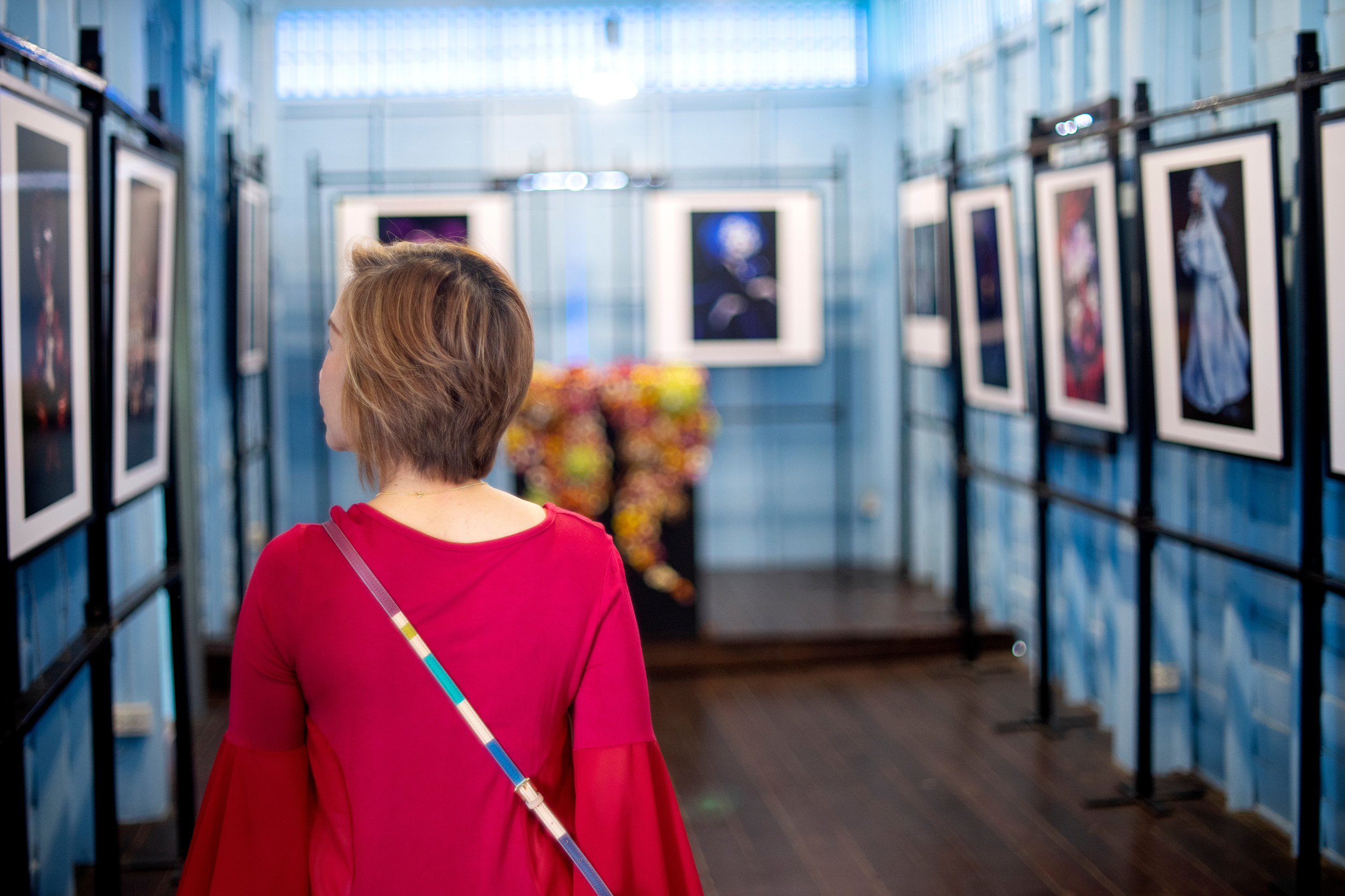 Eine Frau in einem roten Kleid betrachtet gerahmte Kunst in einer Galerie