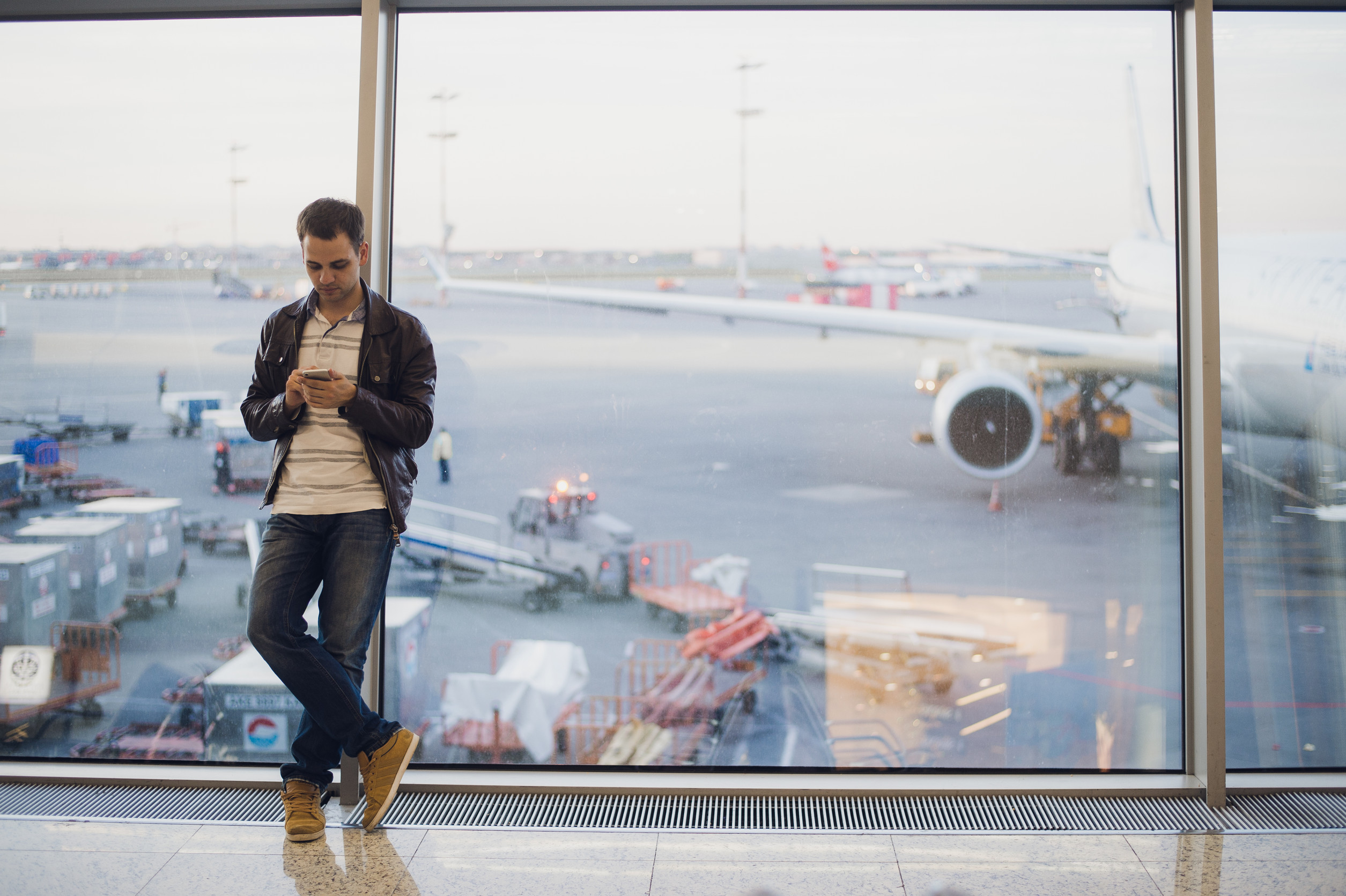 Man using phone at airport window with airplane in background