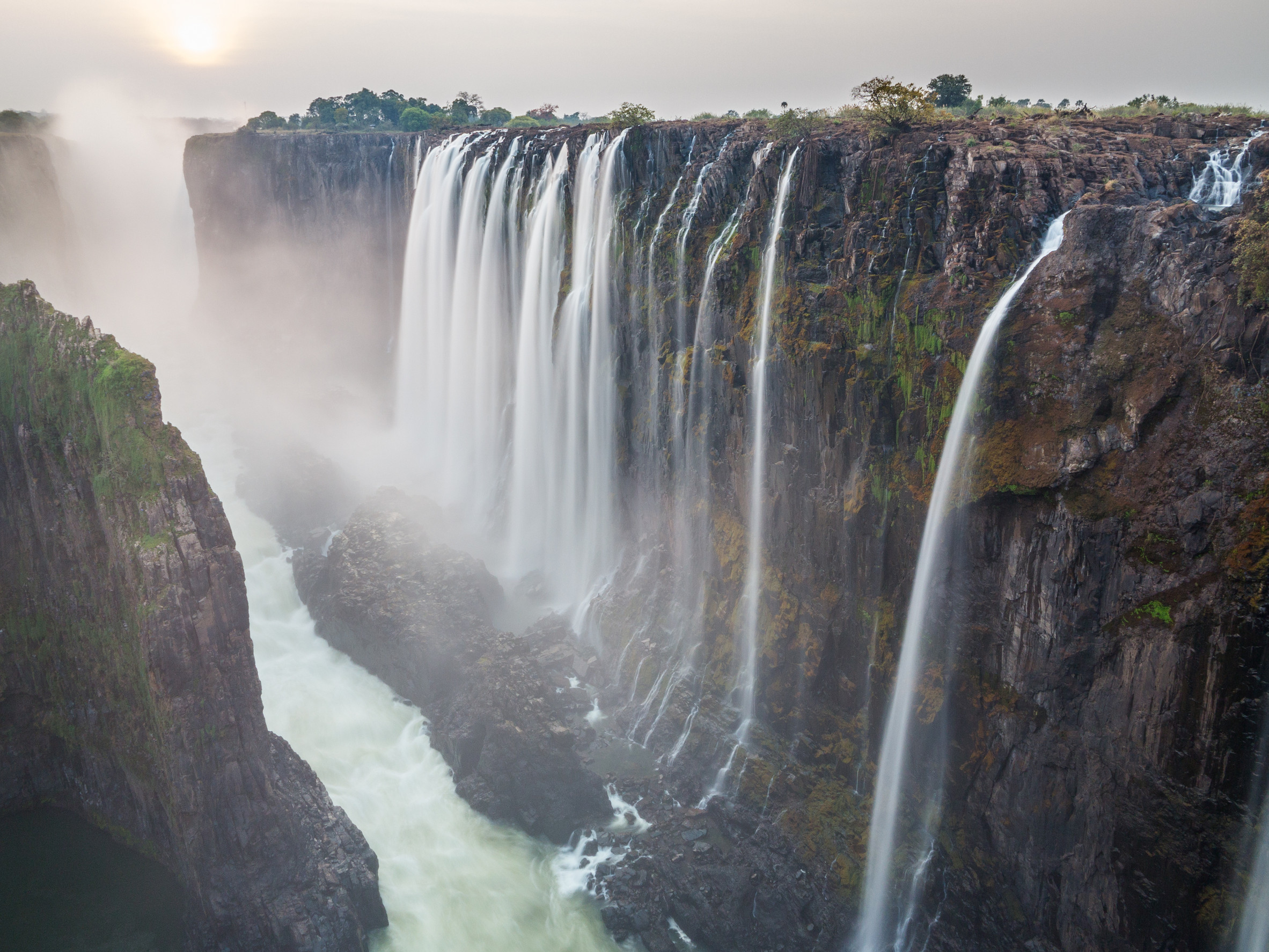 Coucher de soleil sur les chutes Victoria, côté Zambie avec le fleuve Zambèze, soleil rouge, longue exposition