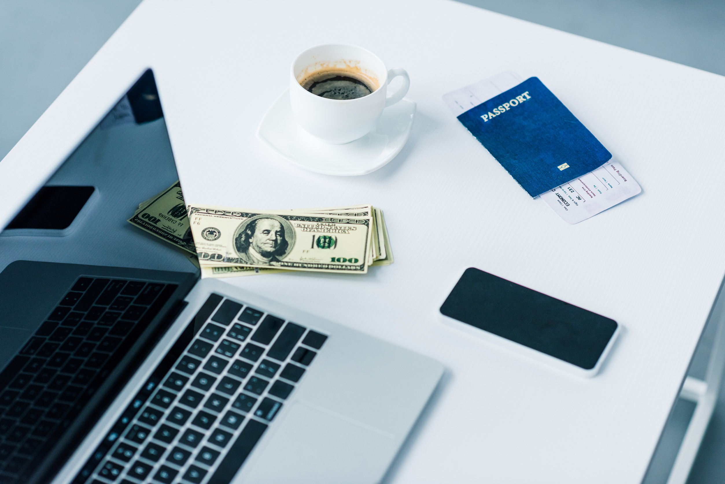 A laptop, a passport, a coffee cup, and a smartphone on a table