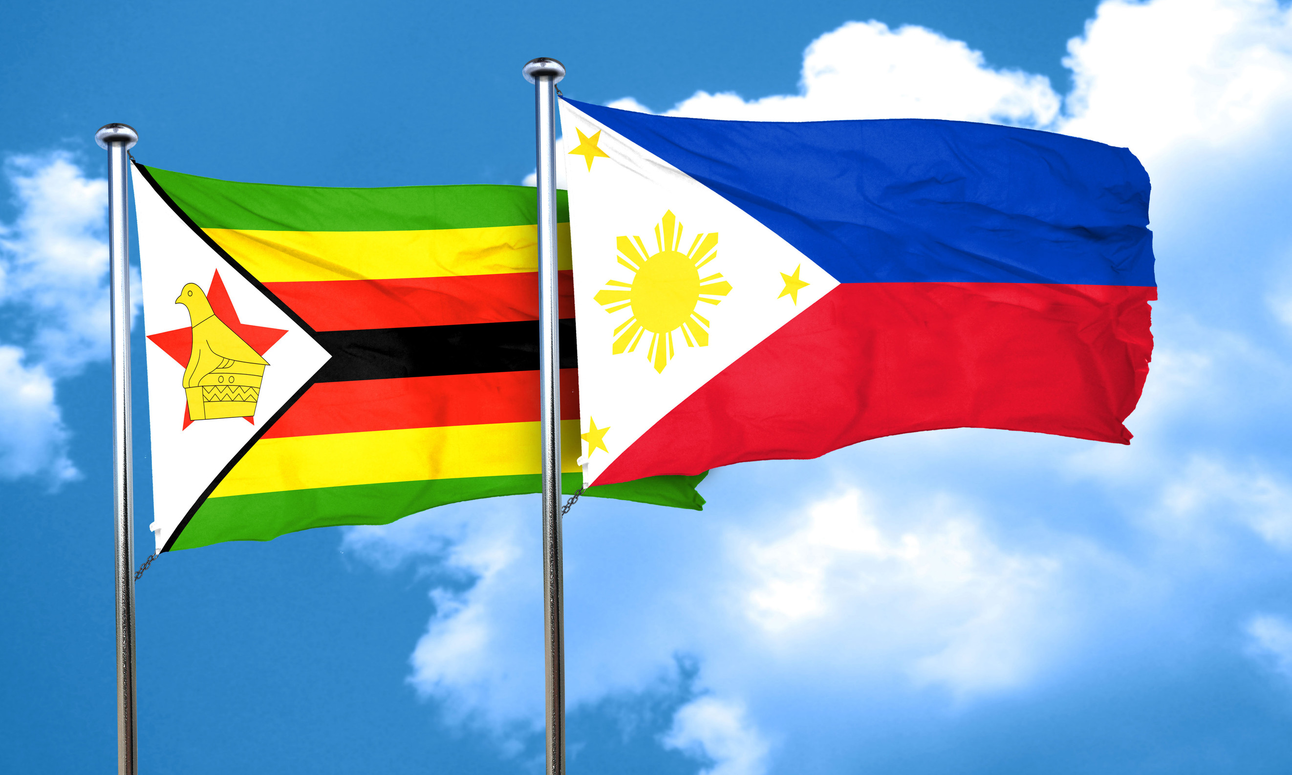 The flags of Zimbabwe (left) and the Philippines (right) blowing side-by-side in a light breeze against a blue sky with fluffy white clouds